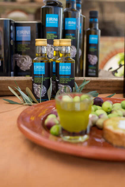 A shot glass filled with olive oil on a plate with olives and bread, in front of our products